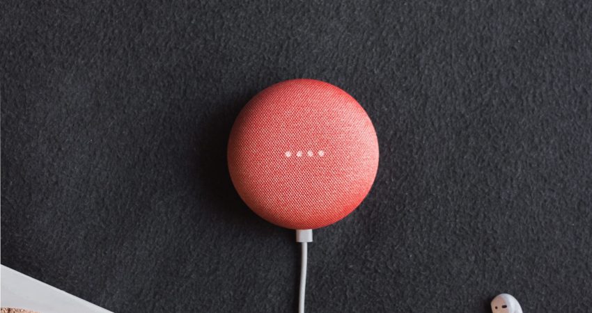 flat lay photography of coral Google Home Mini on black surface beside Apple AirPods